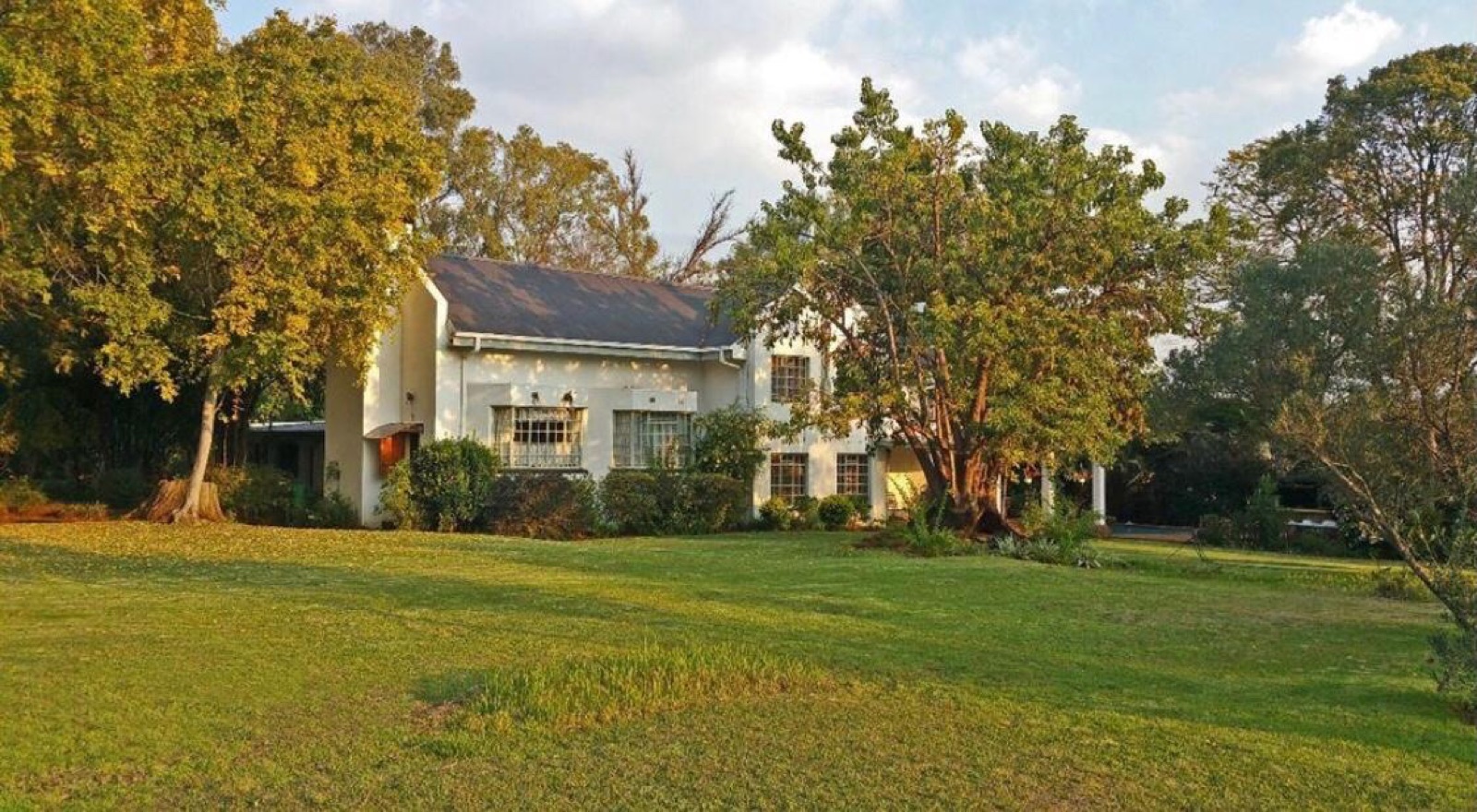 The main building at Ballyteran &middot; Cape-Dutch 2-storey, mature trees and open lawn at golden hour